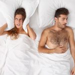Pár az ágyban. A depressziós fiatal nő párnával takarja be a fülét, nem tud aludni a férfi horkolása miatt, álmatlan éjszakája van, ingerülten fekszik az ágyban. Család, lefekvés, álmatlanság, alvási